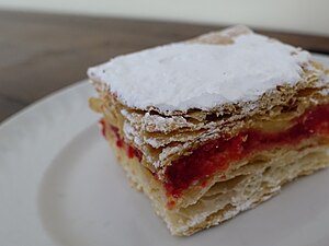 Ein Stück Blätterteig-Biskuitteig-Schichttorte "Torta Diplomatica" auf einem weißen Teller. Sie ist mit Puddingcreme gefüllt.