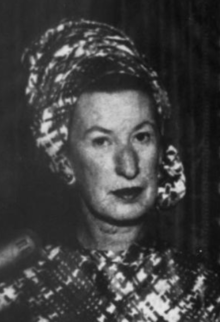 A middle-aged white woman, wearing a print turban and matching dress