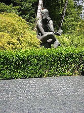 Horisontal gravstein som sier "JAMES JOYCE", "NORA BARNACLE JOYCE", GEORGE JOYCE" og "...ASTA OSTERWALDER JO...", alle med datoer. Bak steinen er en grønn hekk og en sittende statue av Joyce som holder en bok og grubling.