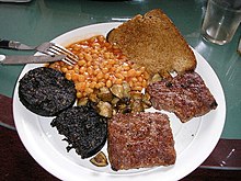 Scottish-style cooked breakfast, centred around black pudding (left), served with square sausage, baked beans, mushrooms, and fried bread Grinners breakfast.jpg
