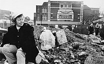 Black and white photograph of Joan Littlewood sat on rubble outside the Theatre Royal, Stratford, East London.