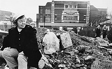 Black and white photograph of Joan Littlewood sat on rubble outside the Theatre Royal, Stratford, East London.