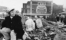 Fotografia in bianco e nero di Joan Littlewood seduta sulle macerie fuori dal Theatre Royal, Stratford, East London