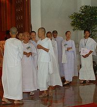 Nove donne asiatiche vestite di bianco sono in piedi e parlano.  Otto sono rasati, uno no.