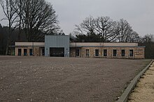 W tle ośrodek zdrowia Saint-Sauveur-en-Puisaye.  Długi, parterowy budynek z wieloma oknami.  Na pierwszym planie pusty parking.