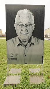 Zu sehen ist eine schwarz-weiß Fotografie die auf einer Wiese in Weimar in einer Metallkonstruktion steht. Naftali Fürst trägt kurzes helles Haar und trägt eine Brille.