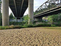 A small sandy river beach with concrete bridges overhead