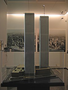 世贸中心模型的照片。中央一左一右为两座八英尺高的世贸中心模型，周围有几栋低矮的楼房模型，模型外罩着玻璃，背后墙壁上挂着世界贸易中心在曼哈顿下城的大幅照片。