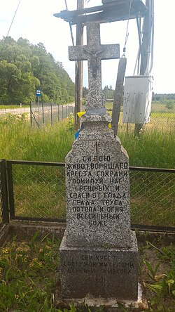 Ortodoks nazar lintas dengan Cyrillic prasasti dari tahun 1960, yang terletak di pintu masuk ke desa dari jalan provinsi. Di latar belakang, ada sebuah halte bus di arah Hajnówka