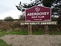 Signboard for the Aberdovey Golf Club with the Welsh language name added on a wooden board underneath.