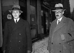 Photo noir et blanc en plan américain de deux hommes dans la rue en manteau et chapeau