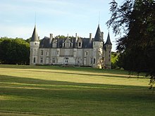 Fotografia a colori di un castello sullo sfondo di un prato punteggiato di alberi.