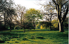 Foto van het park in het vroege voorjaar: de bladeren beginnen net aan de bomen te verschijnen.