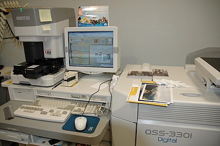 A Noritsu QSS-3301 digital minilab printer. To the left of the monitor is a separate film scanner that is on top of the minilab, but can also be placed anywhere close to it. It sends images from film into the computer through cables. Digital minilab printers have a computer and computer monitor that handle the images before printing, and controls the minilab Noritsu Koki QSS-3301Digital.jpg