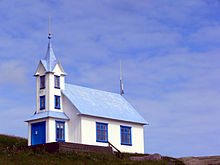 Kerk met witte muren en blauw dak, aan de kant van een heuvel, afgetekend tegen de lucht.