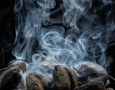 White smoke rising from charcoal briquettes as they start to catch fire and burn