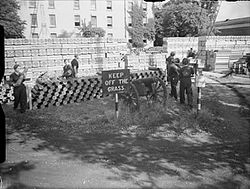 World War II: stacks of brass propellant cartridges along with tin boxes for bagged propellant charges are piled up on the front lawn of the Officers' Residence. The Royal Navy during the Second World War A24937.jpg