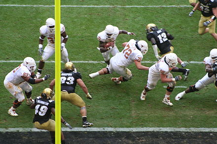 Vince Young of the Texas Longhorns (ball carrier in top center) rushing for a touchdown. A portion of the end zone is seen as the dark strip at the bottom. The vertical yellow bar is part of the goal post.