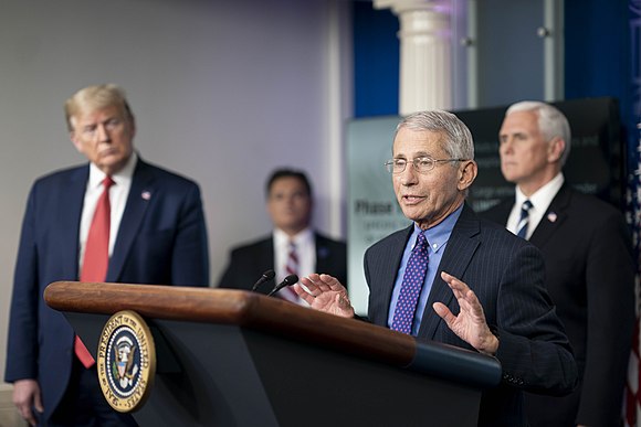 Fauci speaks to the White House press corps on COVID-19 in April 2020, watched by President Donald Trump (left) and Vice President Mike Pence (right).