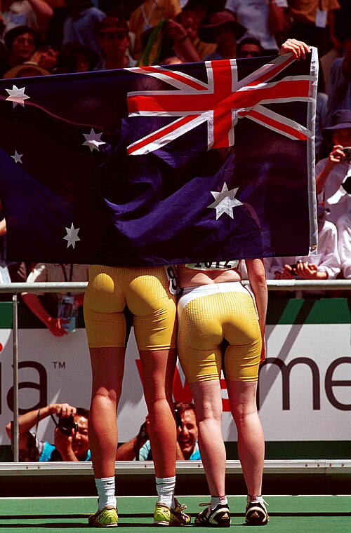 Australian track athletes Katrina Webb (left) and Alison Quinn (right), seen from behind with the Australian flag, celebrate with the crowd over their