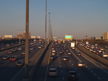 "A traffic jam on a 14-lane freeway, taken from a highway overpass on a clear day. The highway disappears into the distance, surrounded by suburban development on either side."