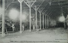 Carte postale ancienne en noir et blanc représentant des personnages dans un bâtiment agricole.