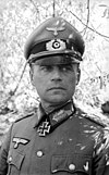 A man wearing a military uniform, peaked cap, and an Iron Cross displayed at the front of his uniform collar.