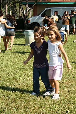 Two children stand side by side, connected by a tie at the ankle.