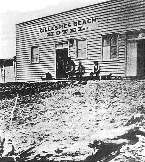 Plain wooden box-shaped weatherboard building, several men sitting outside, signboard on front.