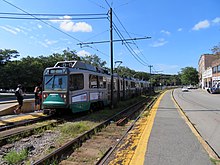A green line train on a sunny day stops at Packard's Corner.