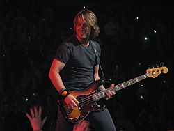 Мужчина с длинными светлыми волосами играет на бас-гитаре
