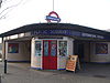 A white-tiled building with a dark blue, rectangular sign reading "LEYTONSTONE STATION PUBLIC SUBWAY LEYTONSTONE STATION" in white letters