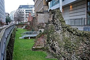 Photograph of ruins of the London Wall between a street and office buildings.