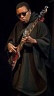 Black woman wearing sunglasses and playing guitar.