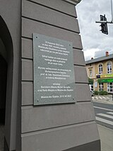 Na zdjęciu widać fragment wieży ratusza z tablicą pamiątkową koloru szarego, na której widnieje napis w języku polskim