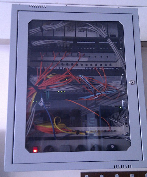 A wall-mount cabinet containing optical fiber cables. The yellow cables are single mode fibers; the orange and aqua cables are multi-mode fibers.