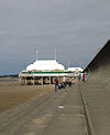 Courte jetée au-dessus du sable, surmontée d'un pavillon blanc avec des mâts de drapeau.