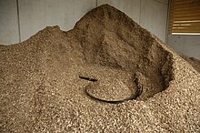 Wood chips in a storage hopper, in the middle an agitator to transport the material with a screw conveyor to the boiler Raumaustragung Hackschnitzel.JPG