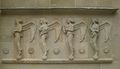 Das Hauptportal der katholischen de:St. Fideliskirche (Stuttgart) in Stuttgart wird von zwei Hochreliefs mit je vier musizierenden Engeln flankiert. Die zum Portal gewandten Engel sind mit großen, weit ausladenden Flügeln dargestellt, tragen fußlange Gewänder und ihr Haupt ist verhüllt oder zeigt einen lockigen Haarschopf. Sie „schweben“ mit den Zehenspitzen ihrer nackten Füße auf Kugeln, die auf einer Zickzackleiste ruhen. Das Traufgesims über ihren Köpfen schützt sie vor Regen. Zwischen den Engeln sind Rundmedaillons angeordnet, die in einem doppelten achtzackigen Stern christliche Symbole bergen. Die Abbildung zeigt die rechte Relieftafel. Attribute der Engel von rechts nach links: saxophonförmiges Instrument, waschbrettartiges Instrument, Fidel, Panflöte. Symbole von rechts nach links: brennende Kerze, Christusmonogramm XP, Rose, Buchstabe Ω. Die Buchstaben Alpha und Omega sind das Symbol für Christus als Anfang und Ende (Offenbarung des Johannes 22, 13). Die Symbolreihe der linken Relieftafel endet mit dem Buchstaben A.