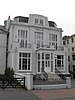 A grey-painted two-storey building with the lower storey set forward and topped by a balcony. "Y.M.C.A." is written in large letters below the dormer window in the roof.