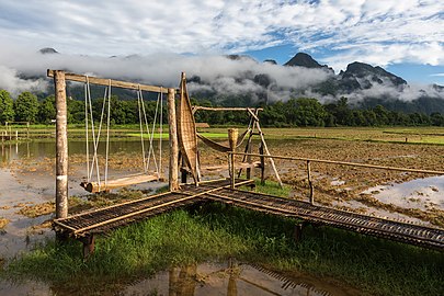 Wooden bench swing and wicker hammocks on a bamboo footbridge in paddy fields a sunny day during the monsoon, Vang Vieng, Laos