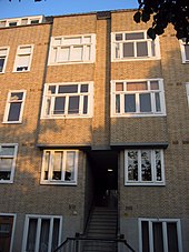 Un immeuble d'appartements en brique de quatre étages montrant la façade du bâtiment, avec plusieurs fenêtres et un escalier intérieur menant à l'immeuble.