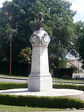 Fotografia colorida de um busto de metal em um pedestal de pedra.