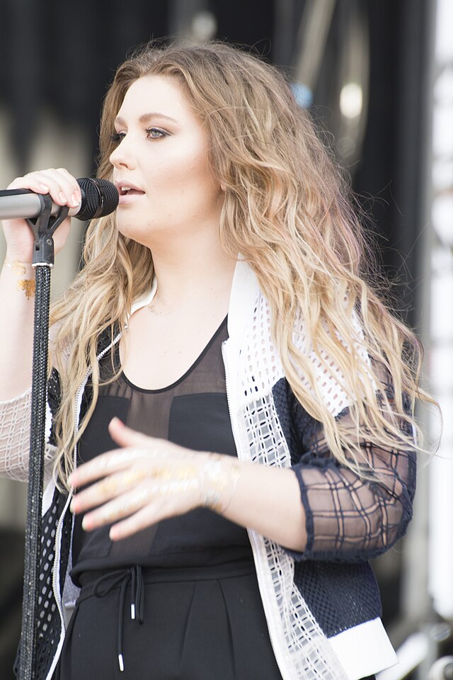 A woman with blonde hair beyond her shoulders. She had one hand on a microphone on stand