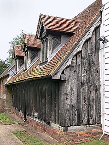 The north wall and part of the west wall of the nave; the notch, low down on the 7th trunk along from the corner, may either be a "leper's squint", or an Anglo-Saxon window. Greensted Church North Side.jpg