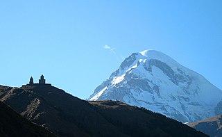 14th-century Georgian Orthodox Gergeti Trinity Church building, with the Mount Kazbek in the background Kazbeghi.jpg