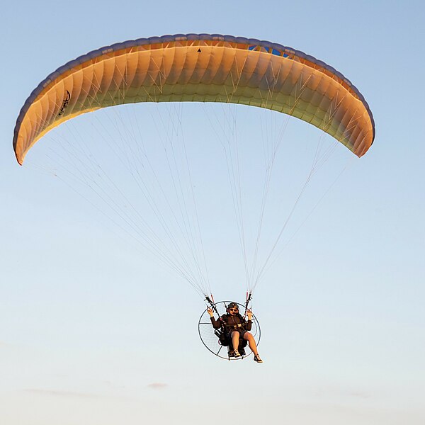 A powered paraglider (paramotor) flies by.