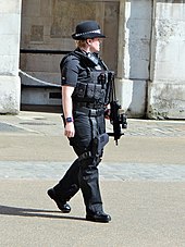 Photographie d'une femme portant une tenue renforcée, une arme et un chapeau.