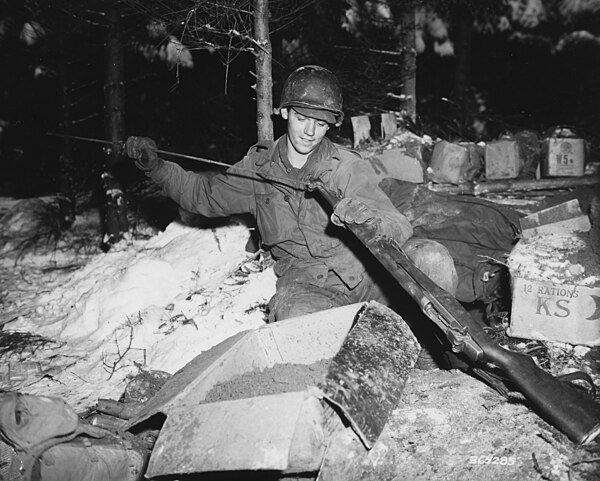 PFC William J. Ottersbach of 3rd Battalion, 327th cleans his rifle during a break near Foy. 11 January, 1945.