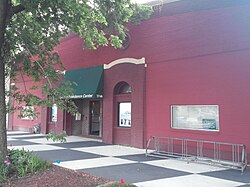 A red brick with green awning building stands before a checkered sidewalk.